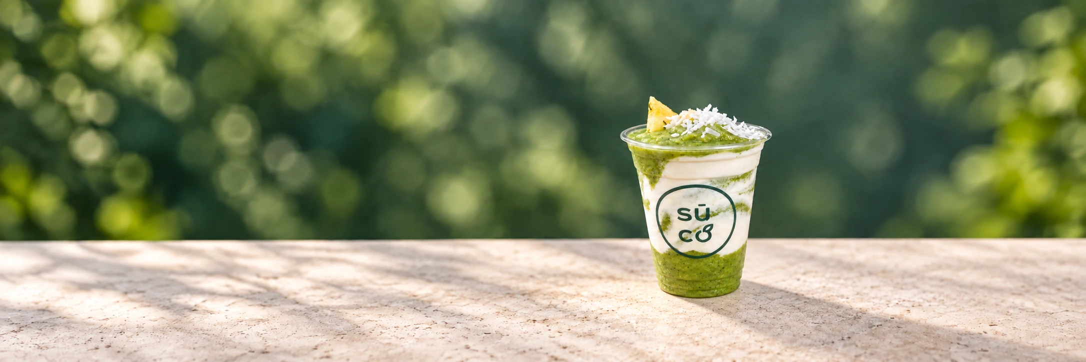 A green Suco smoothie with a creamy swirl and coconut topping